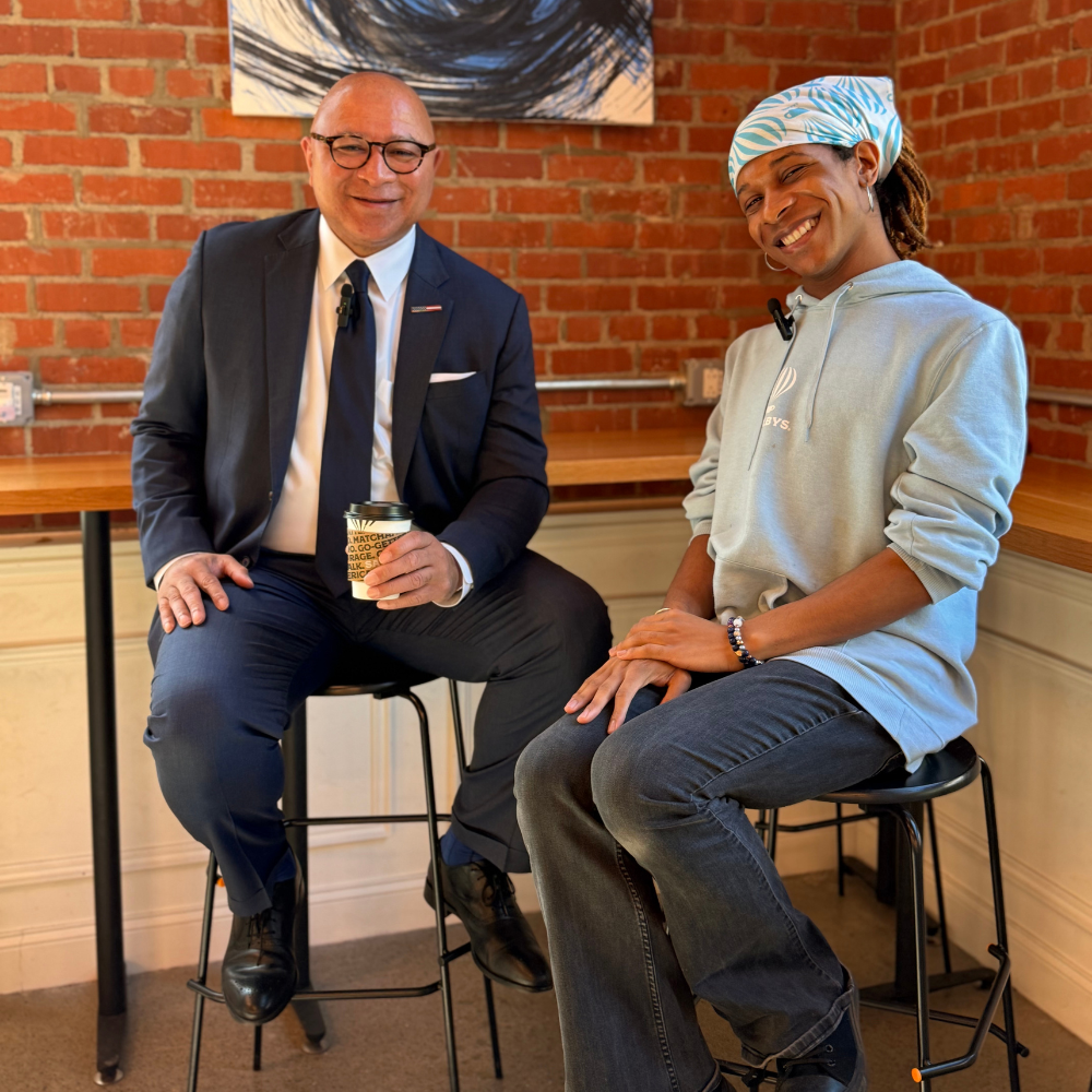 General DeFoor and Margo seated, General holding coffee cup, both smiling and looking at photographer, brick wall background